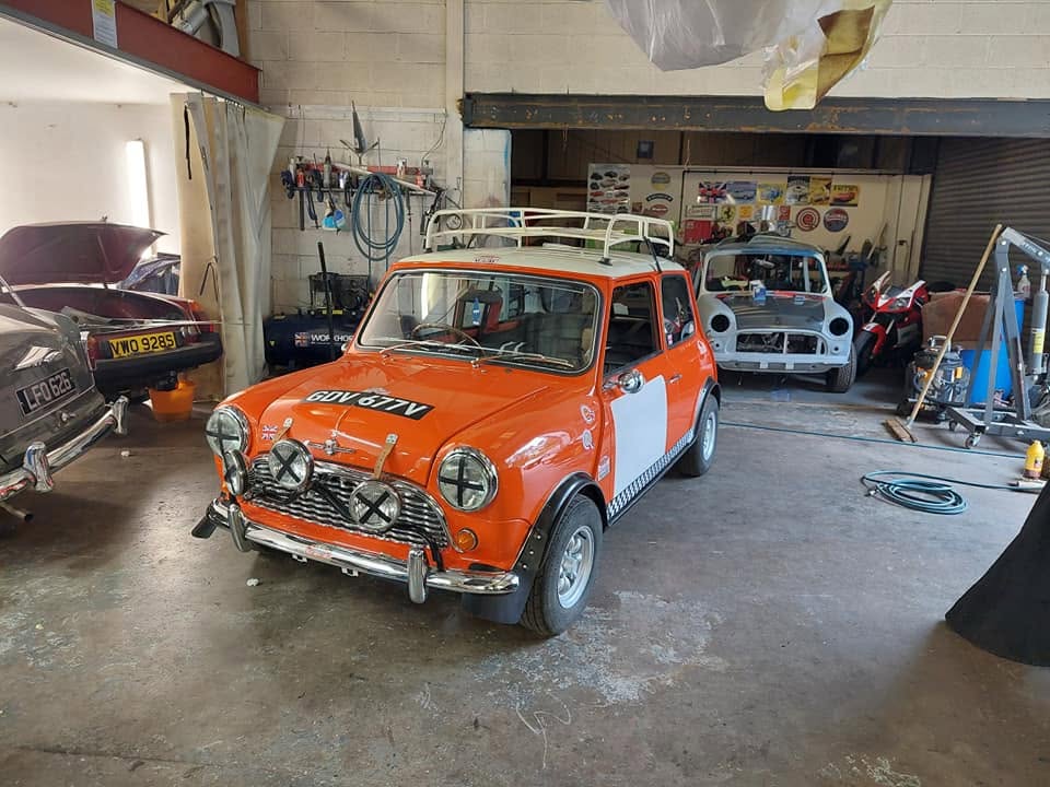 Orange and white Mini with roof rack in a workshop
